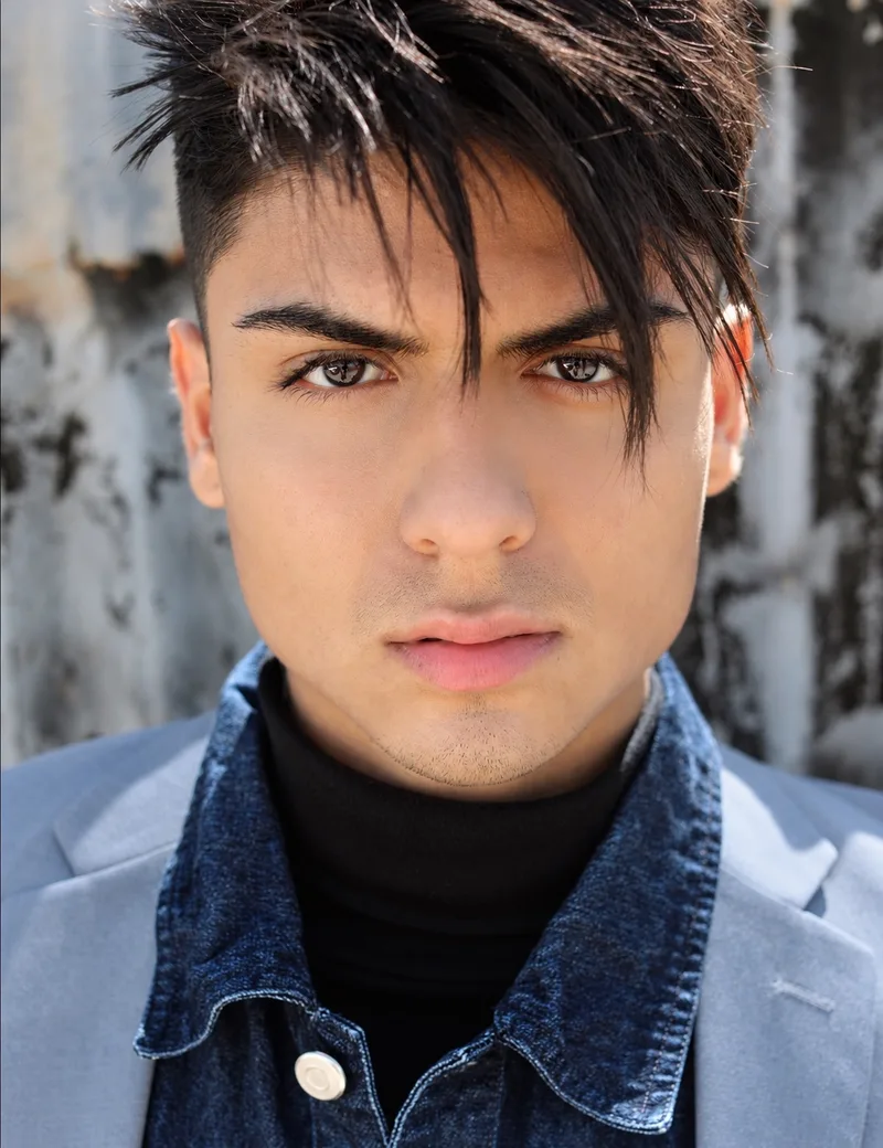 Natural-light headshot in a denim jacket and light blazer against a textured wall