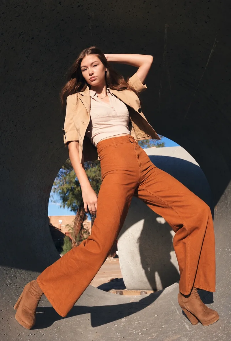 Full-length outdoor fashion portrait in orange trousers and a beige jacket framed by concrete curves