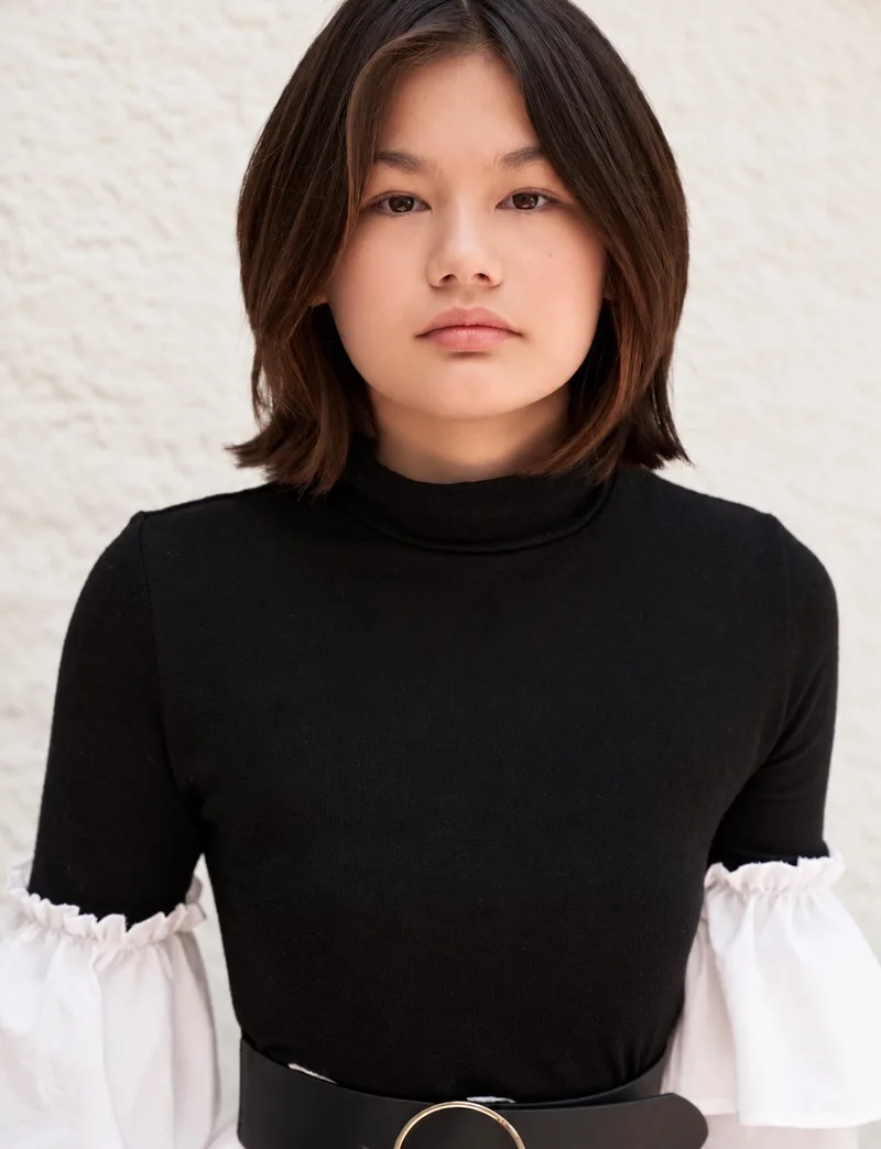 Portrait in a black top with white sleeves against a cream textured wall