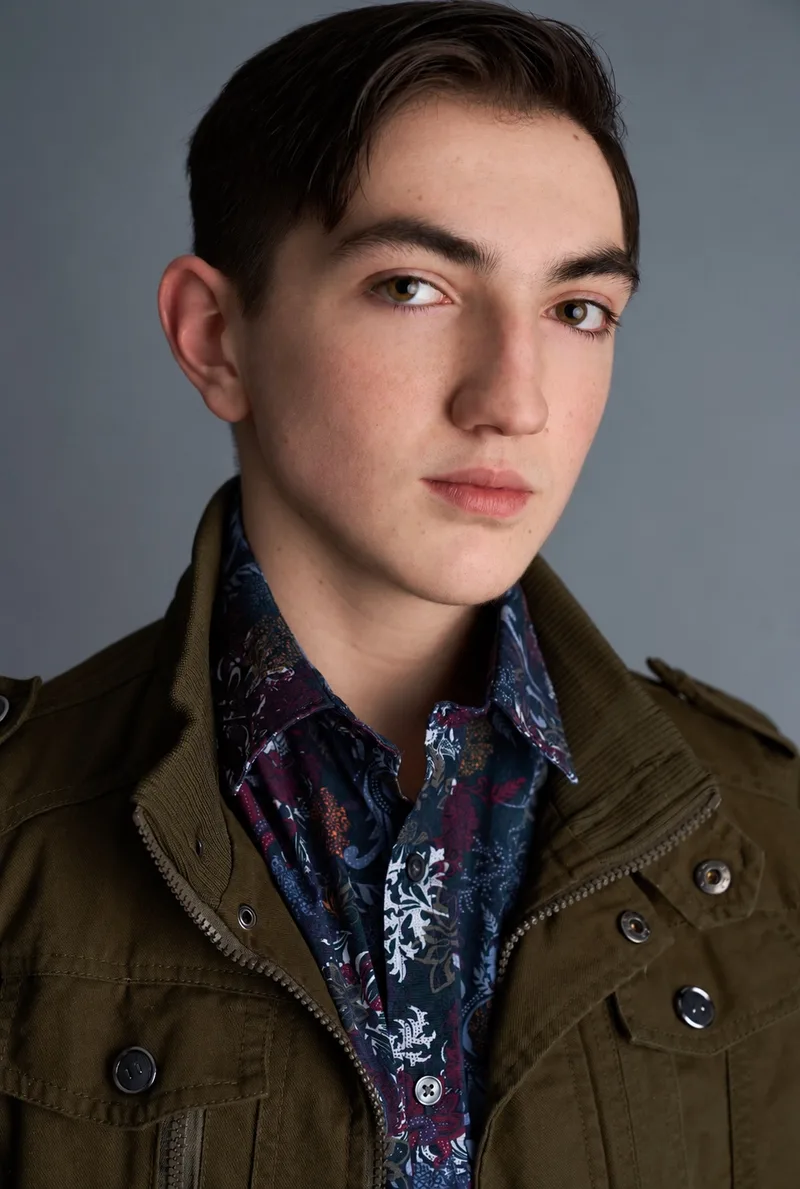 Studio headshot in a patterned shirt and dark jacket against a gray background