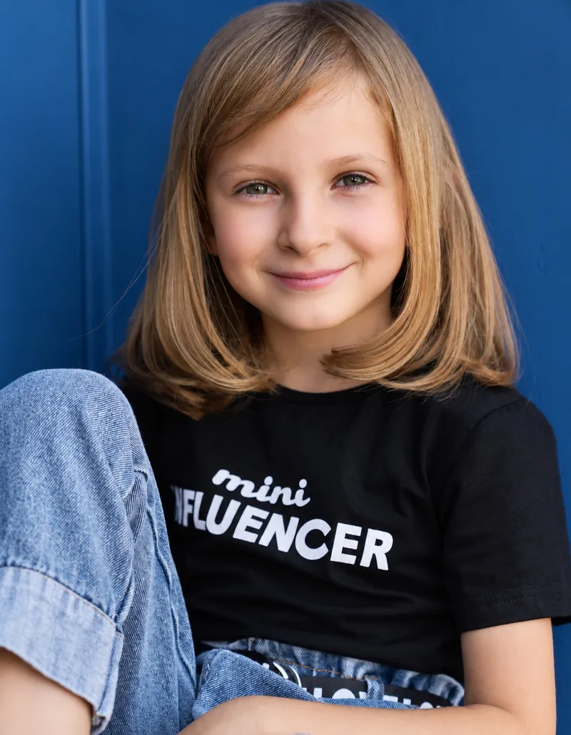 Smiling young performer in a black T-shirt and jeans seated against a blue door